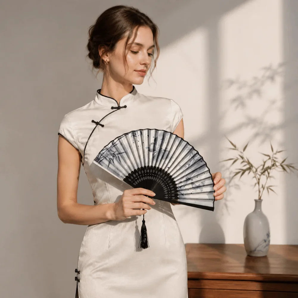 A woman holds an antique style bamboo folding hand fan in a white dress against a light background.