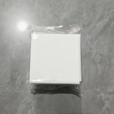 A white square storage holder for a scale with a self-adhesive mount, packaged in clear plastic.