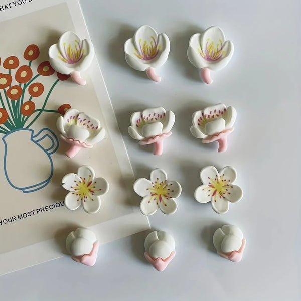 A collection of twelve white and pink resin flower fridge magnets arranged on a light background.