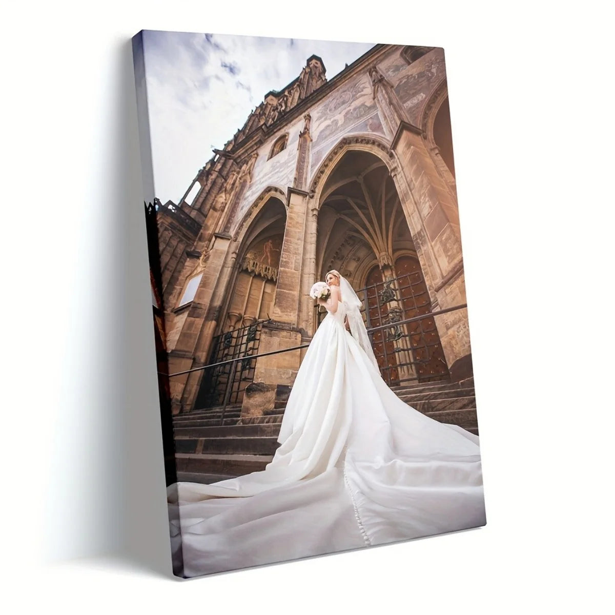 A vertical canvas print of a grand stone archway and cathedral facade with a bride in a white wedding dress standing in the f