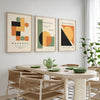 Three framed abstract geometric canvas prints featuring orange, black, and olive green shapes on a white background.