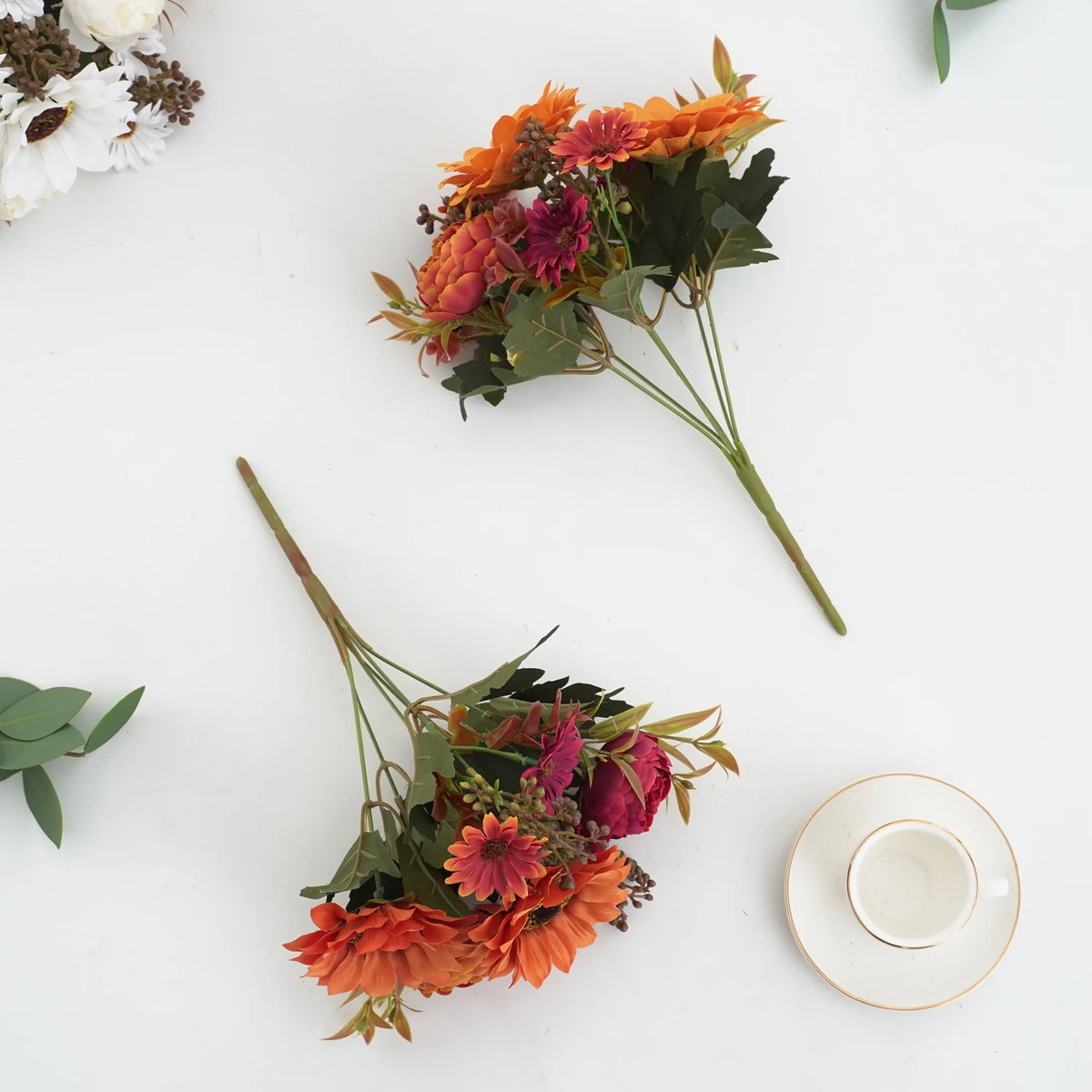 Un bouquet de fleurs artificielles orange et rouge profond, incluant des tournesols et des pivoines, arrangé sur une surface 