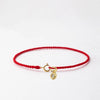 A handmade red string bracelet with a gold plated clasp is displayed against a white background.