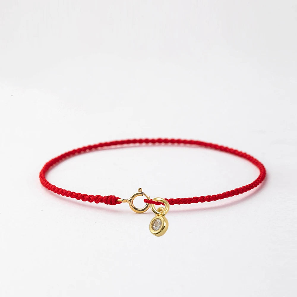 A handmade red string bracelet with a gold plated clasp is displayed against a white background.