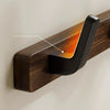 A close-up of a dark walnut wood coat rack with a curved hook and storage shelf mounted on a light wall.