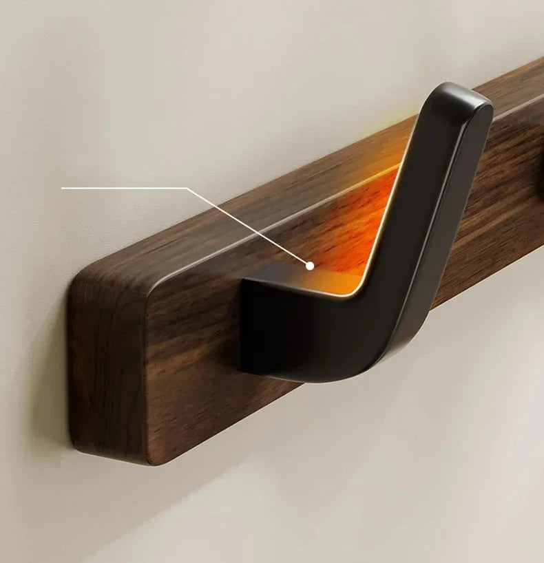 A close-up of a dark walnut wood coat rack with a curved hook and storage shelf mounted on a light wall.