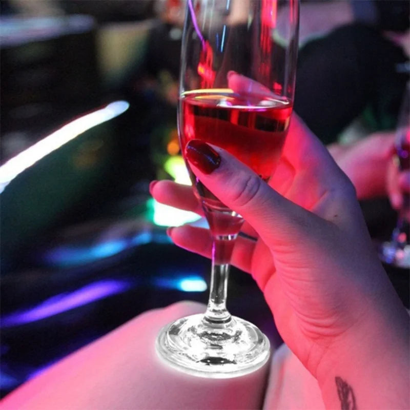 A hand holds a glass of red wine illuminated by luminous LED coaster lights.