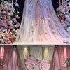 A pink satin bow with a long tulle drape is displayed as event decor, featuring floral accents.