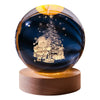 A dark blue crystal ball decoration featuring a laser engraved silhouette of a person standing next to a Christmas tree.