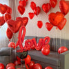 Eine Anordnung roter herzförmiger Ballons und eines großen roten Glitzer-Liebeszeichens auf einem Sofa.