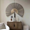 A large, fan-shaped wall decor made of woven bamboo strips with a tassel hanging on a light gray wall.