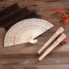 Hand carved bamboo folding fan with intricate floral patterns resting on a wooden surface.