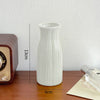 A white ceramic bud vase with vertical ridges sits on a wooden surface.