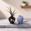 A set of eight mini resin vases with floral patterns, including a dark purple vase and a light blue vase, displayed on a gray
