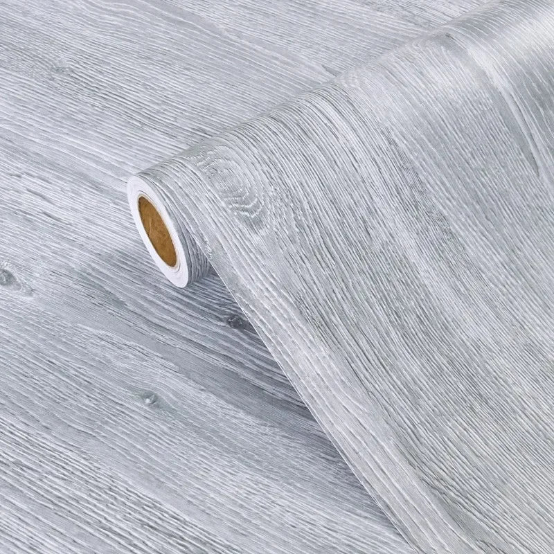 Roll of self-adhesive PVC wallpaper film with a wood grain texture, showing the rolled edge.