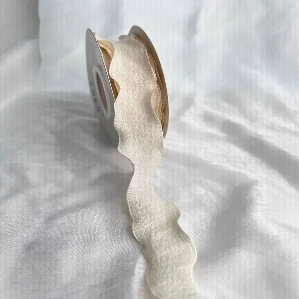 A roll of cream colored decorative fishtail yarn ribbon is shown against a white background.