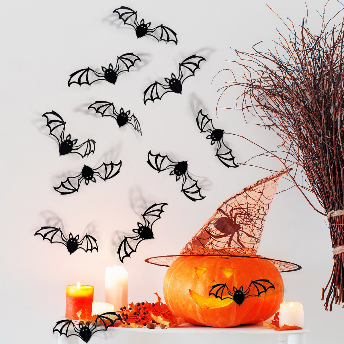 A carved pumpkin decoration with bat silhouettes and a bundle of dry branches on a white surface.