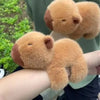 A fluffy capybara animal wristband and ring is being held up by a person's hand.