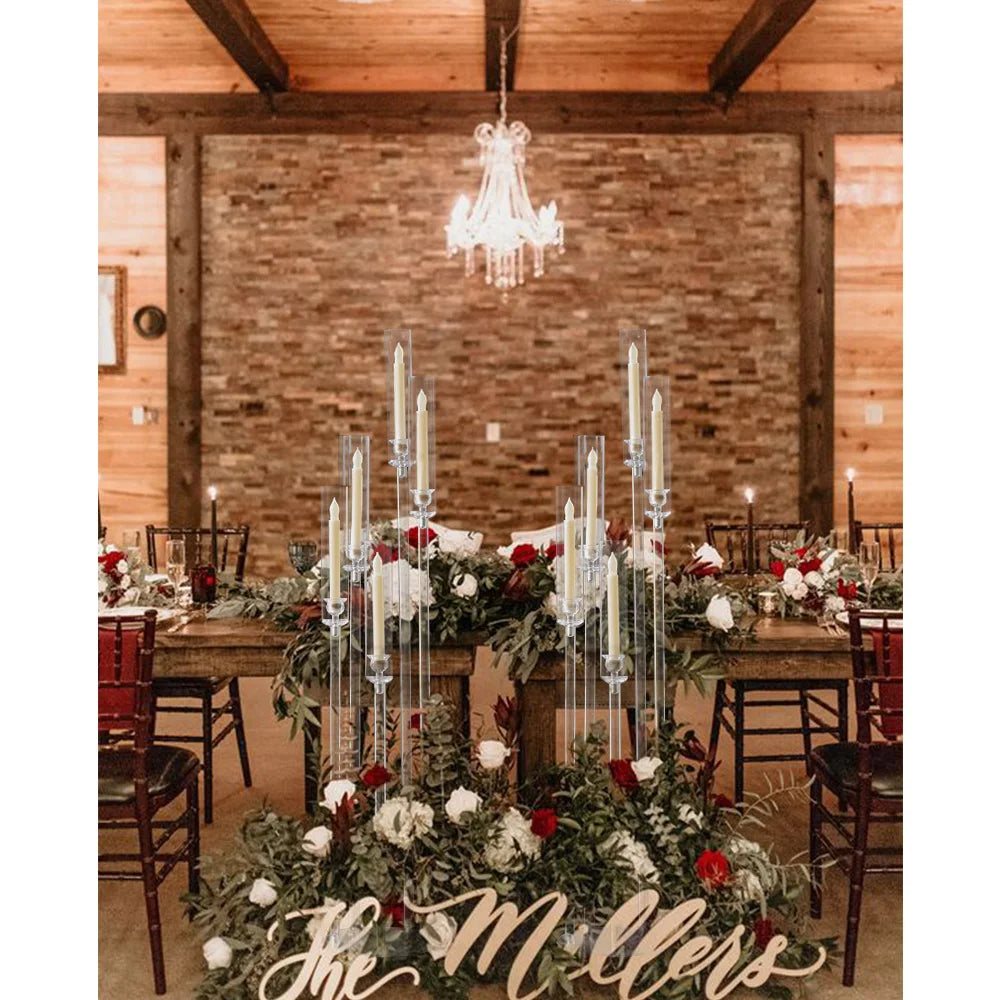 A rustic wedding table decorated with greenery and red roses featuring tall acrylic candelabras.