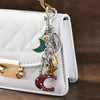 A silver keychain featuring a teal crescent moon charm and a red glitter crescent moon charm attached to a white quilted leat