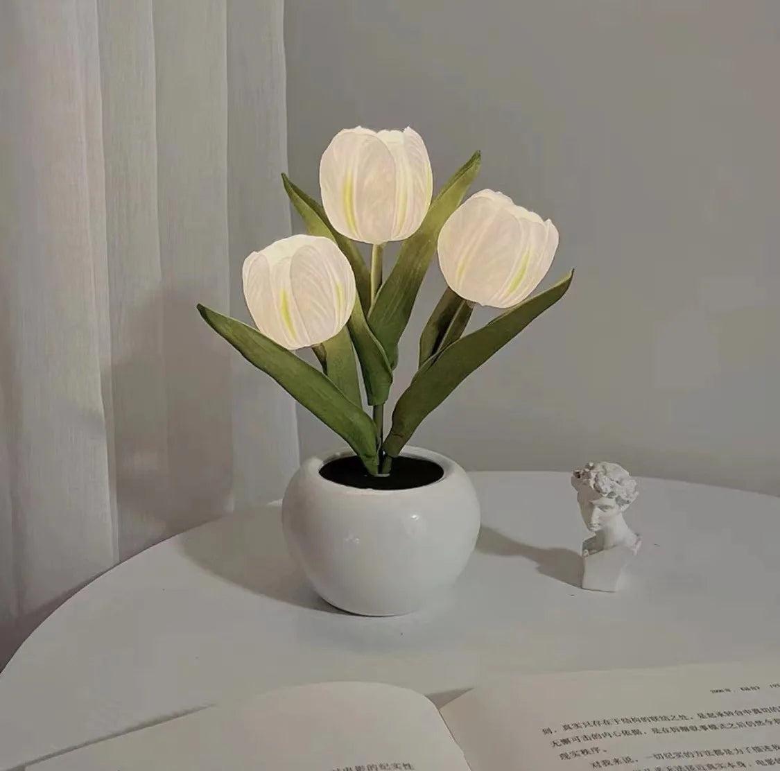 A white LED tulip night light with delicate petals growing in a smooth ceramic pot.