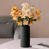 Ein Strauß orangefarbener und cremefarbener Blumen in einer gerippten schwarzen Keramikvase.
