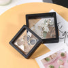 A black display box holds a pair of silver dangle earrings and a set of silver rings on a light background.