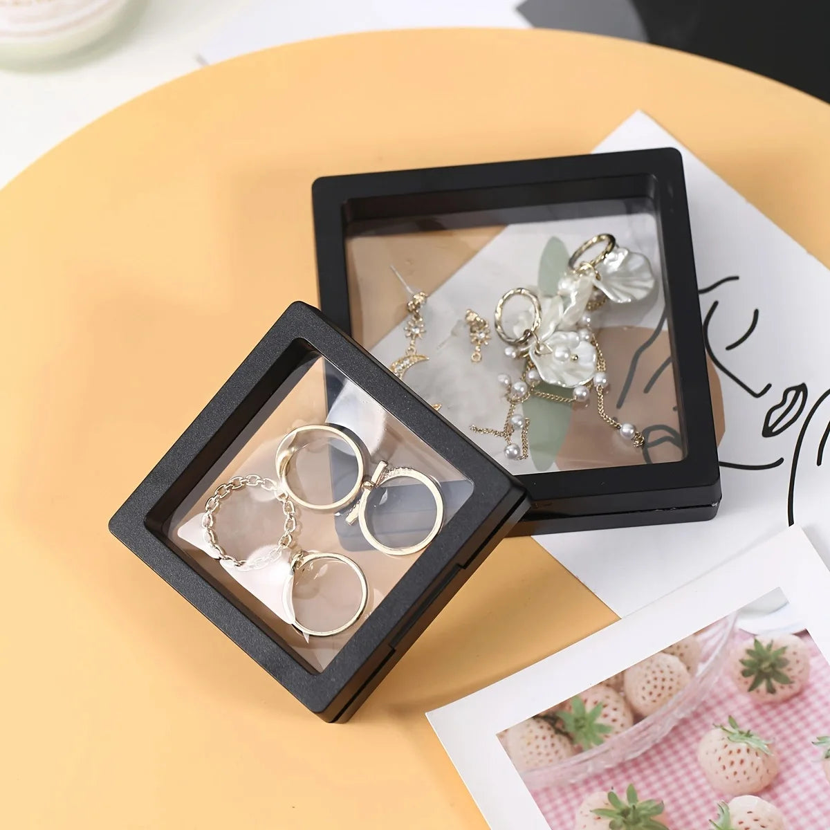 A black display box holds a pair of silver dangle earrings and a set of silver rings on a light background.