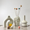 A set of three white geometric vases with dried floral elements displayed on a light surface.