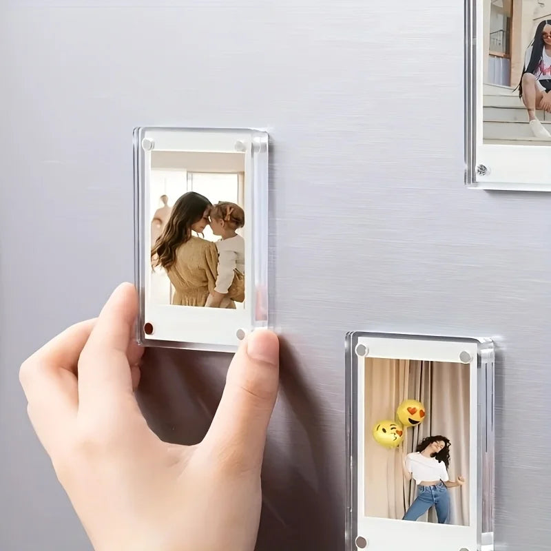 A hand holds a magnetic acrylic picture frame displaying a photo of a mother and child on a refrigerator surface.