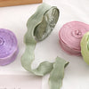 Rolls of decorative fishtail yarn ribbon in shades of green and pink on a white surface.