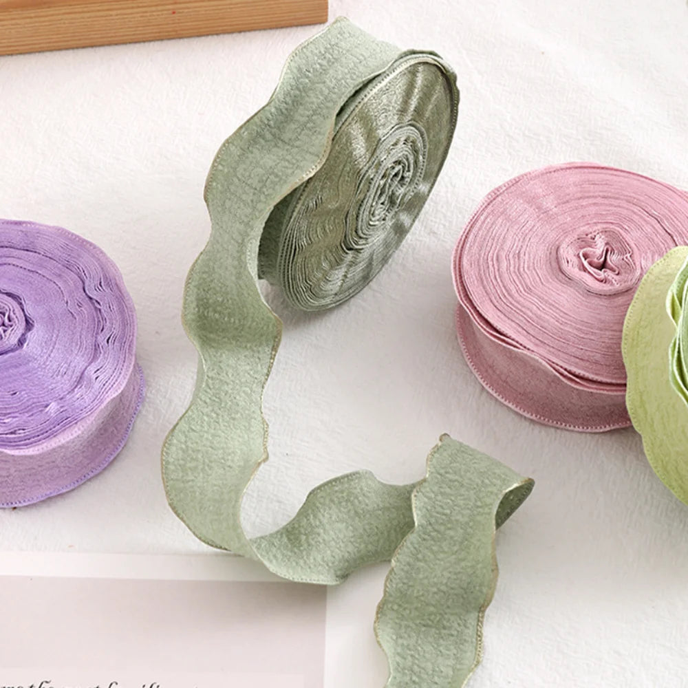 Rolls of decorative fishtail yarn ribbon in shades of green and pink on a white surface.