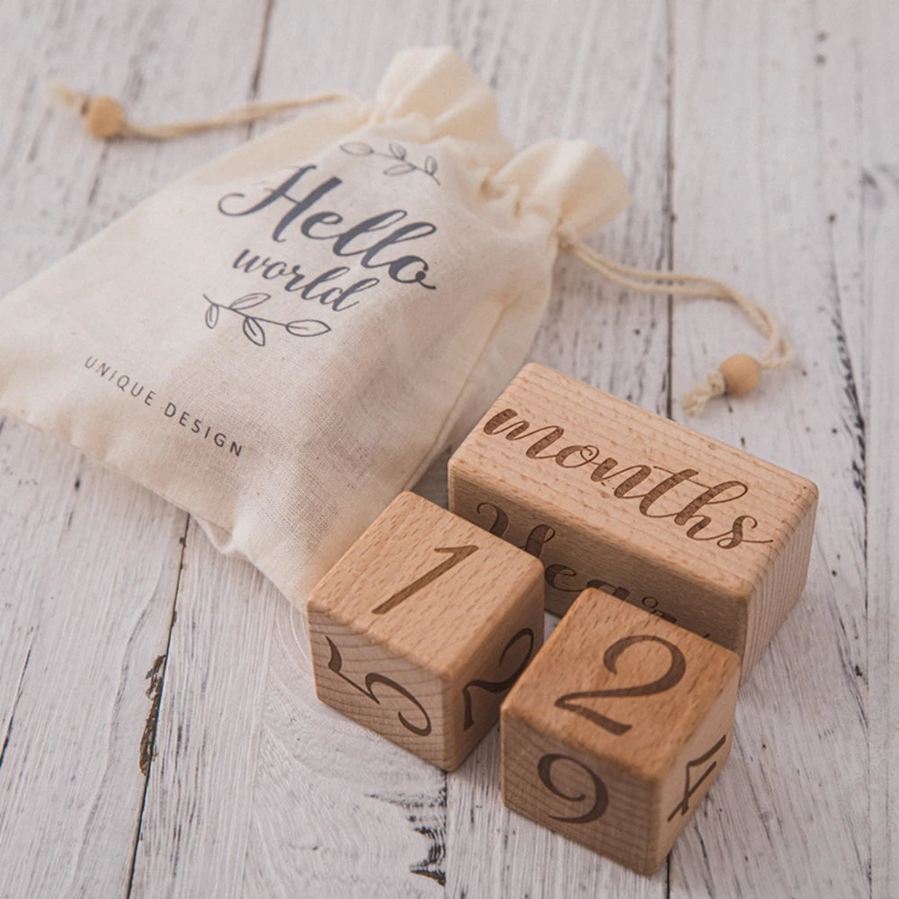 A beige cloth bag with 'Hello world' printed on it next to several wooden baby milestone cards.