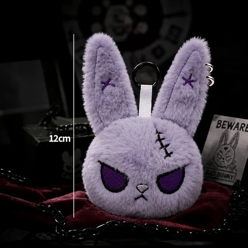 A purple fluffy bunny plush keychain with purple accents is displayed on a dark red fabric.