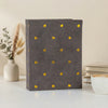 A dark gray photo album with gold foil heart designs rests on a white surface.