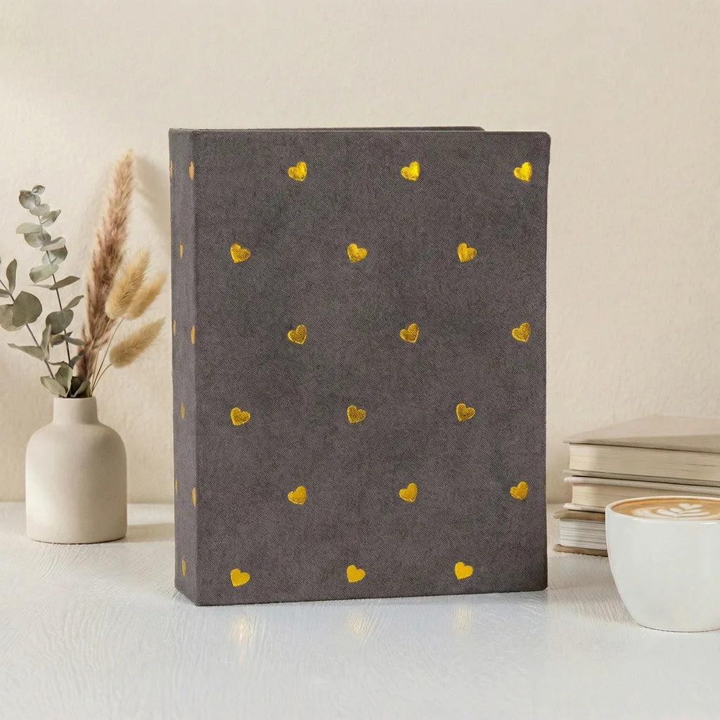 A dark gray photo album with gold foil heart designs rests on a white surface.