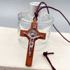 A wooden cross necklace with a silver figure and wax rope cord is displayed against a clear glass bottle.