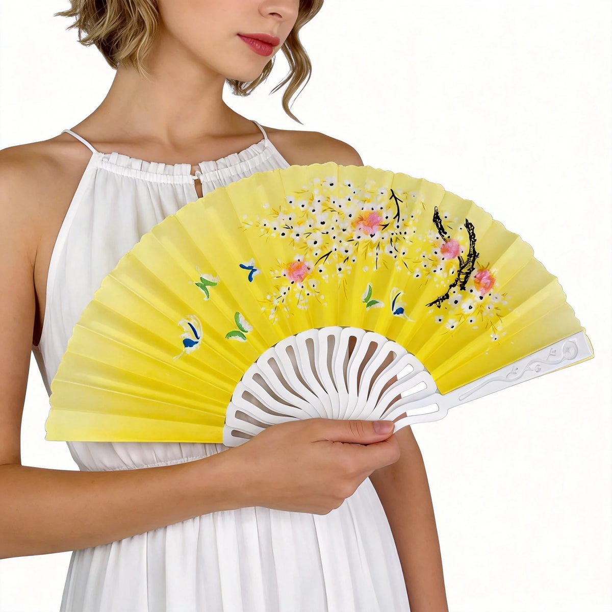 A woman holds a yellow and pink printed plastic folding fan against a white dress.