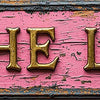 A distressed pink metal sign with the text THE LOO in gold lettering.