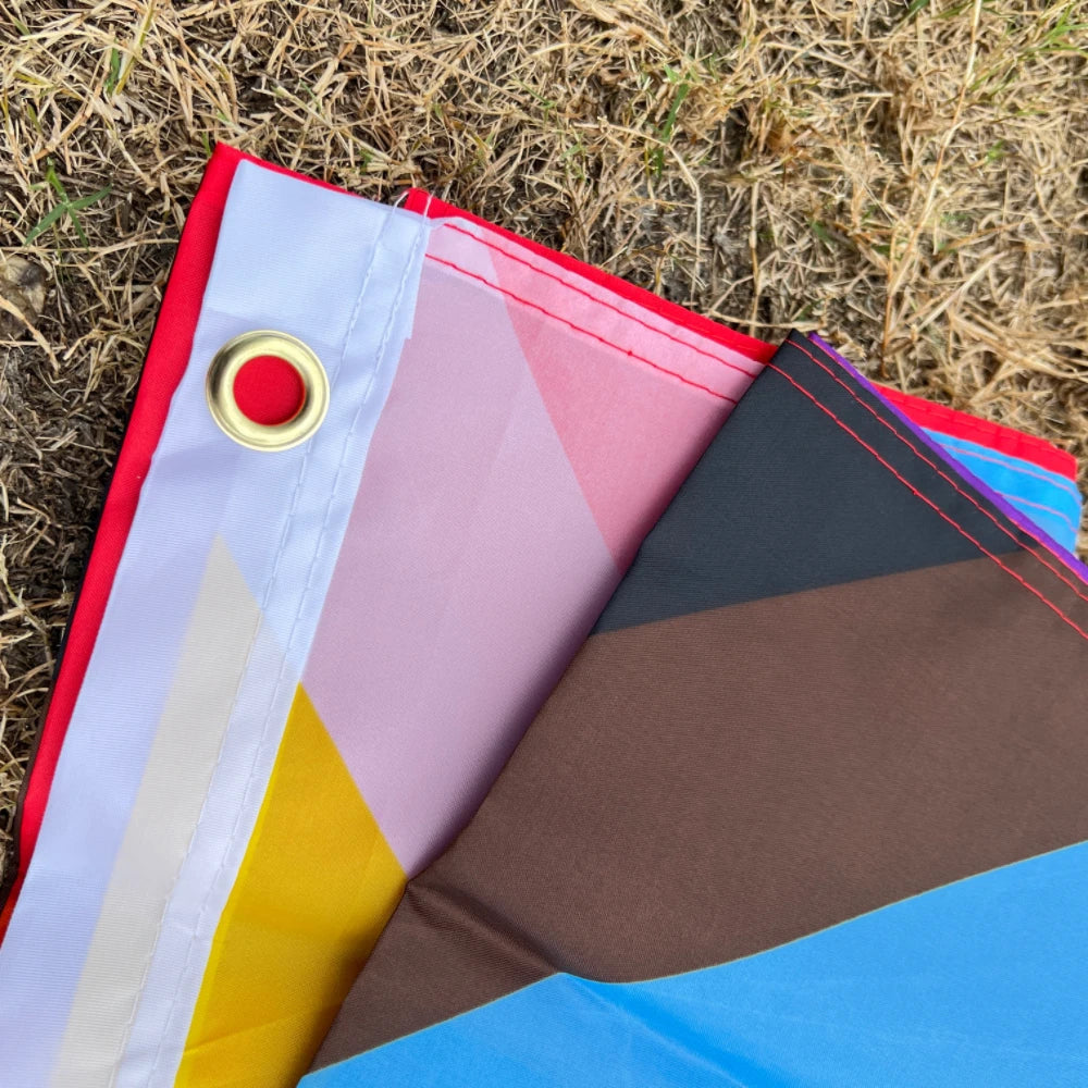A folded Pride rainbow flag banner showing various colors like red, pink, yellow, and blue on a grassy background.