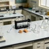 A miniature laboratory set featuring glass tubes, flasks, and small samples on a white countertop.