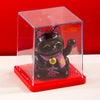 A black cat figurine with pink accents is displayed inside a clear acrylic box on a red base.