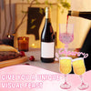A glass of red wine is being poured into a pink wine glass next to a bottle on a wooden table.