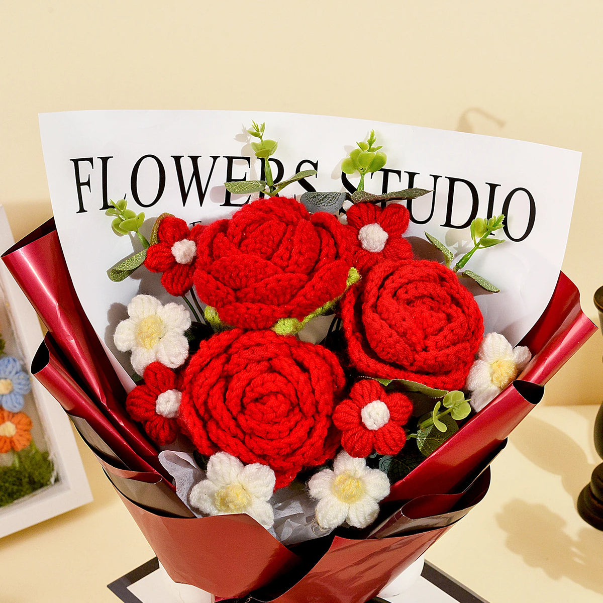 A bouquet of handcrafted red crochet roses with white accents presented in a dark red paper wrapping.