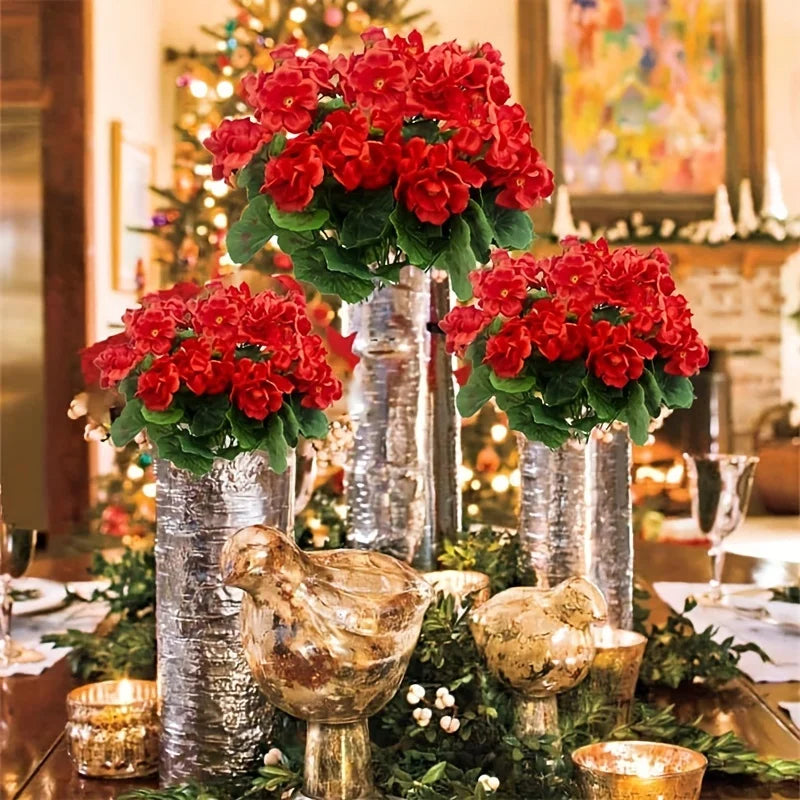 A festive display of bright red artificial geranium flowers in silver vases and greenery for holiday decor.