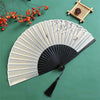 A light gray and white bamboo folding fan with a delicate floral bird print, set against a green background.
