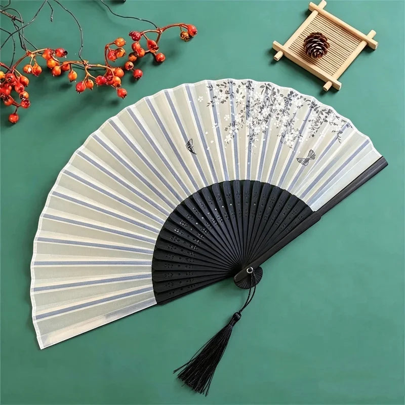 A light gray and white bamboo folding fan with a delicate floral bird print, set against a green background.