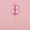 A pink number eight candle with a white stick against a light pink background.