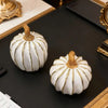 Elegant white and gold resin decorative pumpkins displayed on a dark surface.