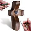 A dark brown wooden comfort prayer cross with a carved heart detail, shown being held by a hand.